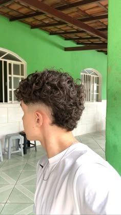 a young man with curly hair standing in front of a green wall and looking off into the distance