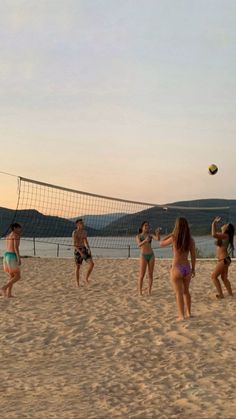 four girls playing volleyball on the beach at sunset