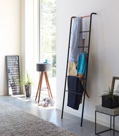 a ladder leaning against the wall with clothes hanging on it and a potted plant next to it