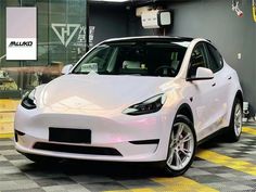 a white tesla electric car parked in a garage with yellow and black checkered flooring