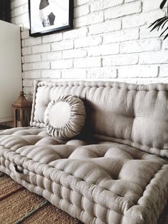 a couch sitting in front of a white brick wall with a round pillow on it