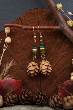 two pairs of pine cone earrings with green and brown beads on them sitting on top of a leaf