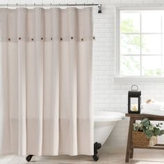 a white shower curtain in a bathroom next to a bathtub with a candle and potted plant