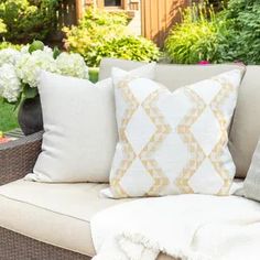 a couch with some pillows on top of it in front of flowers and bushes outside