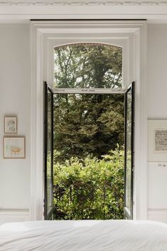 an open window in a white bedroom overlooking the trees and shrubbery on the other side