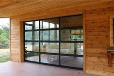 an open garage door on the side of a wooden building with glass doors and windows