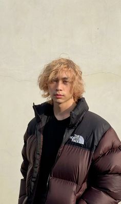 a young man standing in front of a wall wearing a black and brown puffy jacket