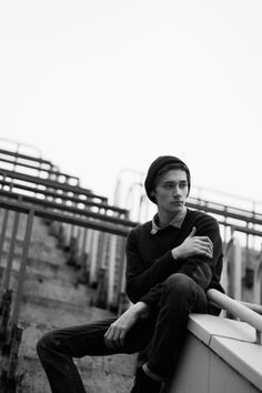 a man sitting on top of a white wall next to a metal rail and some stairs