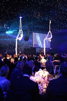 a group of people sitting at tables in a room with lights and decorations on the ceiling