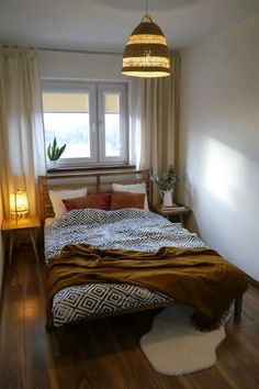 a bedroom with a bed, lamp and window in the corner next to a wooden floor