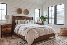 a bed sitting in a bedroom next to two windows and a rug on top of a wooden floor