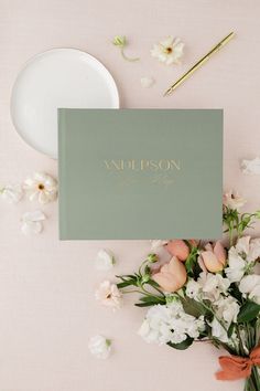 a table topped with flowers next to a white plate and napkin on top of a pink surface