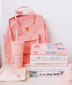 a stack of books sitting on top of a table next to a pink backpack and cup