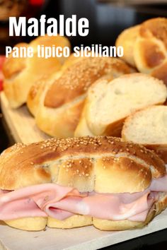 ham and cheese sandwich with bread rolls in the background on a cutting board that says matfade pane tipico siciliano