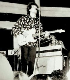 the man is playing his guitar in front of an audience at a music concert while singing into a microphone