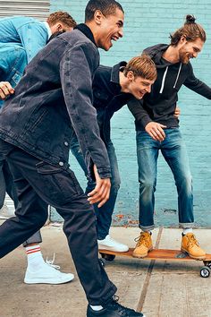 a group of young men riding on top of a skateboard in front of a blue wall