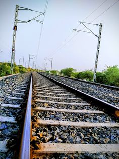 the train tracks are lined with rocks and trees in the distance, as well as power lines above them