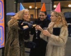 three women in party hats are talking to each other while holding wine glasses and champagne flutes