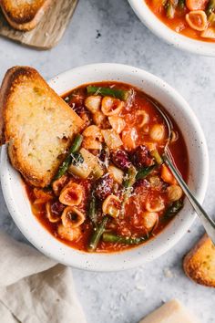 two bowls of pasta soup with bread on the side