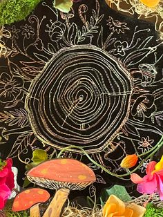 an artistic painting with flowers and mushrooms in the grass on a black board that is surrounded by straw