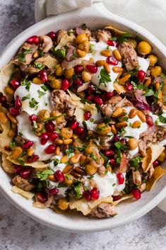 a white bowl filled with nachos topped with meat and pomegranate