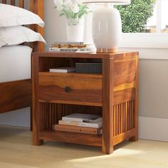 a bed with white pillows and a wooden night stand on top of it next to a window