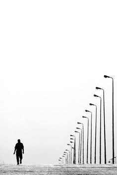 a man is walking down the street in front of many light poles and street lamps