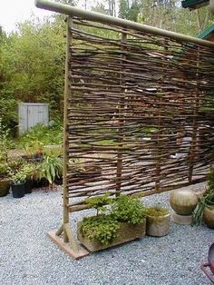 a bamboo fence made out of sticks and potted plants in the middle of a gravel area