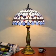 a lamp sitting on top of a wooden table next to a book and cup filled with coffee