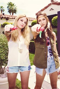 two beautiful young women standing next to each other in front of a house and pointing at the camera