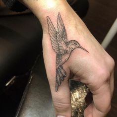 a small hummingbird tattoo on the left hand is shown in black and grey ink