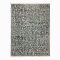 a gray rug with an intricate design and fringes on the bottom, in front of a white background