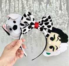 the hand is holding two mickey and minnie mouse headbands, one with a dalmatian face on it