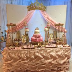 a table topped with a pink cake and lots of gold decorations on top of it