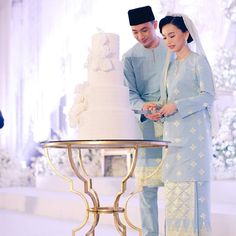 a man and woman standing next to a white cake on top of a metal stand