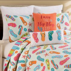 a bed with colorful flip flops on it and an orange pillow that says i love the beach life