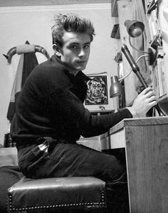 a young man sitting at a desk in front of a computer monitor and keyboard, with various tools on the wall behind him