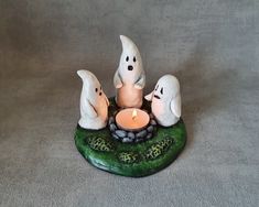 three ghost figurines sitting on top of a rock with a lit candle in the middle