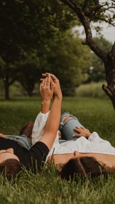 two people laying in the grass with their hands on each other's heads,