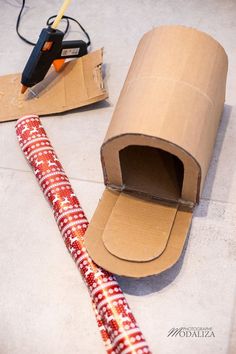 an open cardboard box sitting on the floor next to a red and white patterned tube