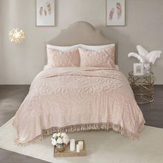 a bed with pink bedspread and pillows in a white room next to pictures on the wall