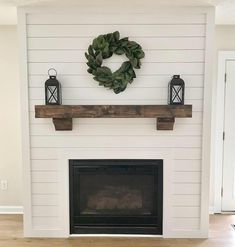 a fireplace with a wreath on the mantle and two lanterns hanging from the mantel