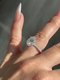 a woman's hand with a diamond ring on top of her finger and white nails