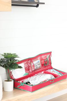 an open red suitcase sitting on top of a table next to a potted plant