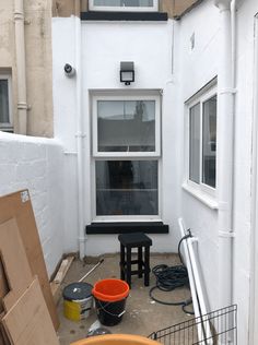 an empty back yard with two buckets on the ground and a window in the corner