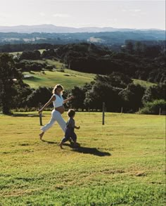 a woman holding a baseball bat while walking next to a little boy on a field