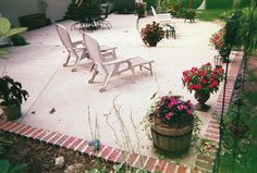 an outdoor patio with chairs and potted flowers on the ground in front of it