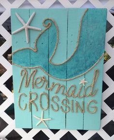 a wooden sign that says mermaid crossing on the side of a fence with starfish