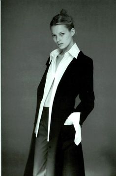 a black and white photo of a woman in a long coat with her hands on her hips