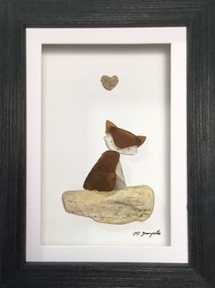 a little dog sitting on top of a rock under a heart shaped object in a black frame